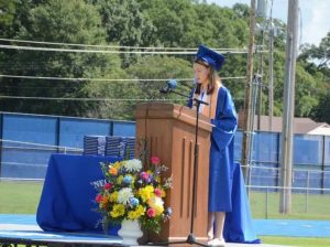 Emily speaks at a podium wearing blue Neodesha High School graduation regalia